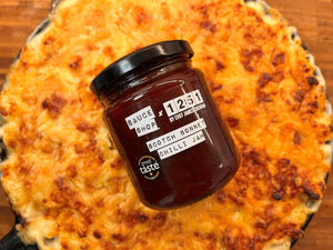 Mac and cheese in a cast iron skillet pan with a Scotch Bonnet Chilli Jam jar placed on top