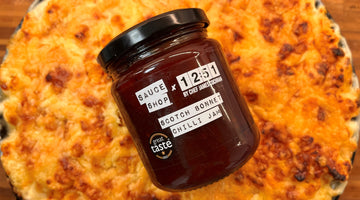 Mac and cheese in a cast iron skillet pan with a Scotch Bonnet Chilli Jam jar placed on top