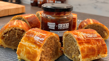 Cut up sausages rolls on a plate, surrounding Sauce Shop Scotch Bonnet Chilli Jam jar