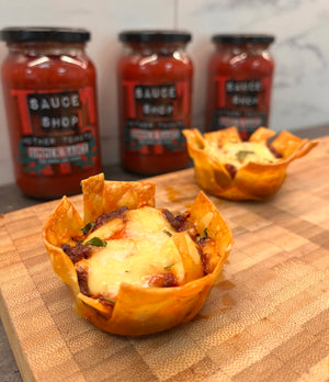 Two lasagne bites on a wooden board with mother tomato simmer sauce in the background