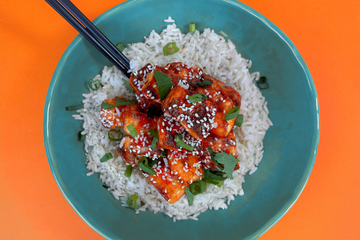 Honey Sriracha paneer bites, on a bed or rice, with chopsticks and a blue bowl.