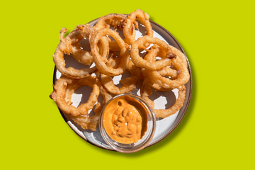 A plate with onion rings piled on top, with a chipotle and lime aioli dip.