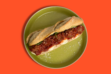 A baguette with saucy meatballs in the middle, all placed on a green plate