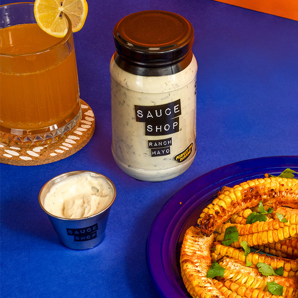 A jar of Sauce Shop Ranch Mayo next to a beverage, a dip pot with ranch mayo inside and sweetcorn ribs